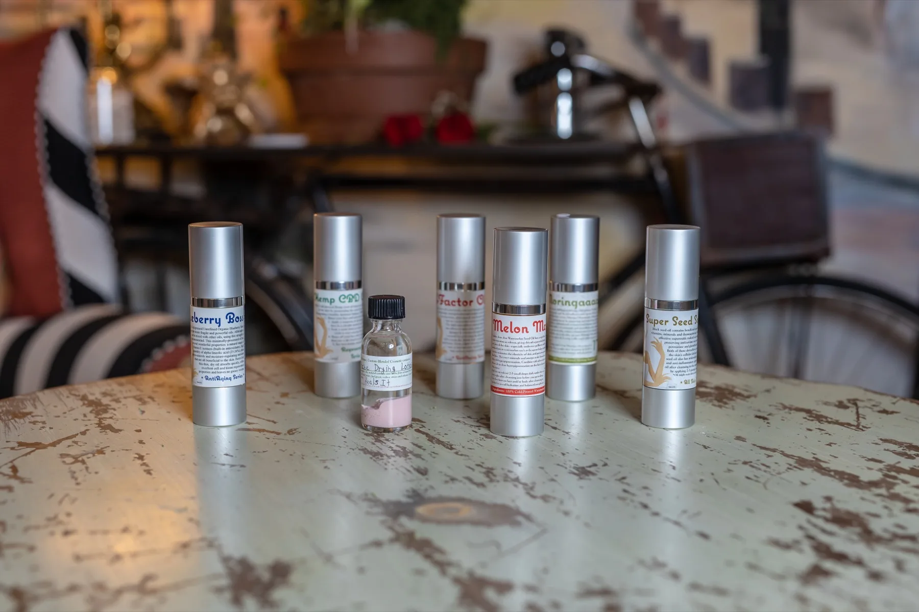 A row of silver airless pump bottles of ESSpa skincare on a weathered painted table in the spa's warm, softly lit lounge