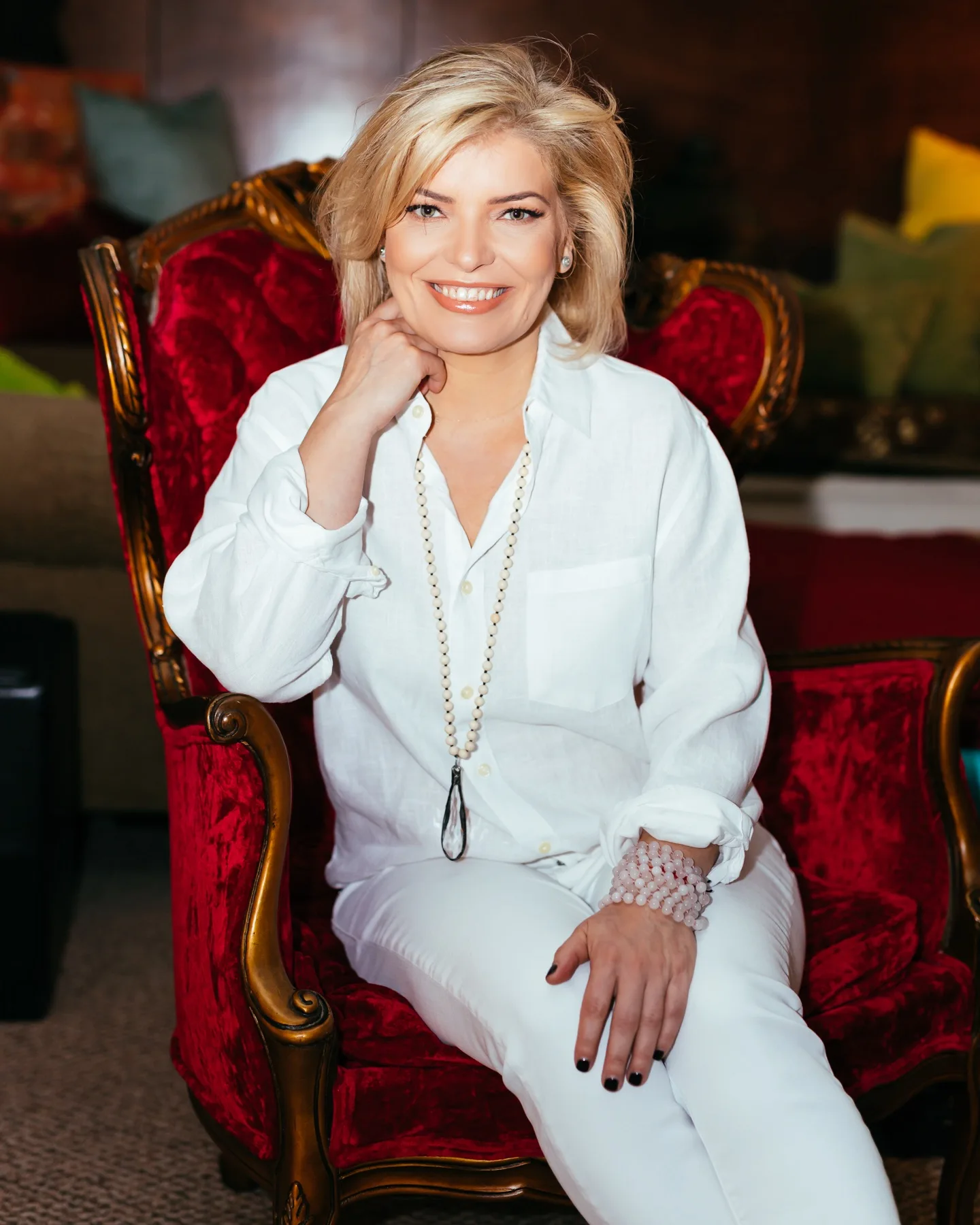 ESSpa founder Eva seated with a warm, welcoming smile in an antique velvet armchair in the spa's lounge