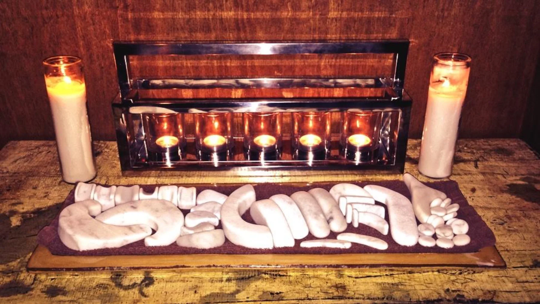 Warm massage stones arranged on a folded towel beside glowing candles at ESSpa Kozmetika in Aspinwall