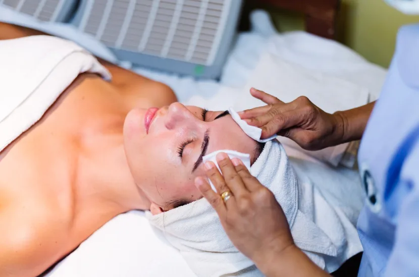 An esthetician's hands pressing soft warm compresses over a guest's freshly cleansed, glowing skin at the close of a facial